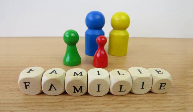 Familie Symbolbild: Spielfiguren in verschiedenen Farben und Größen stehen nebeneinander. Davor liegen Würfel mit Buchstaben darauf. Die Würfel bilden das Wort Familie.