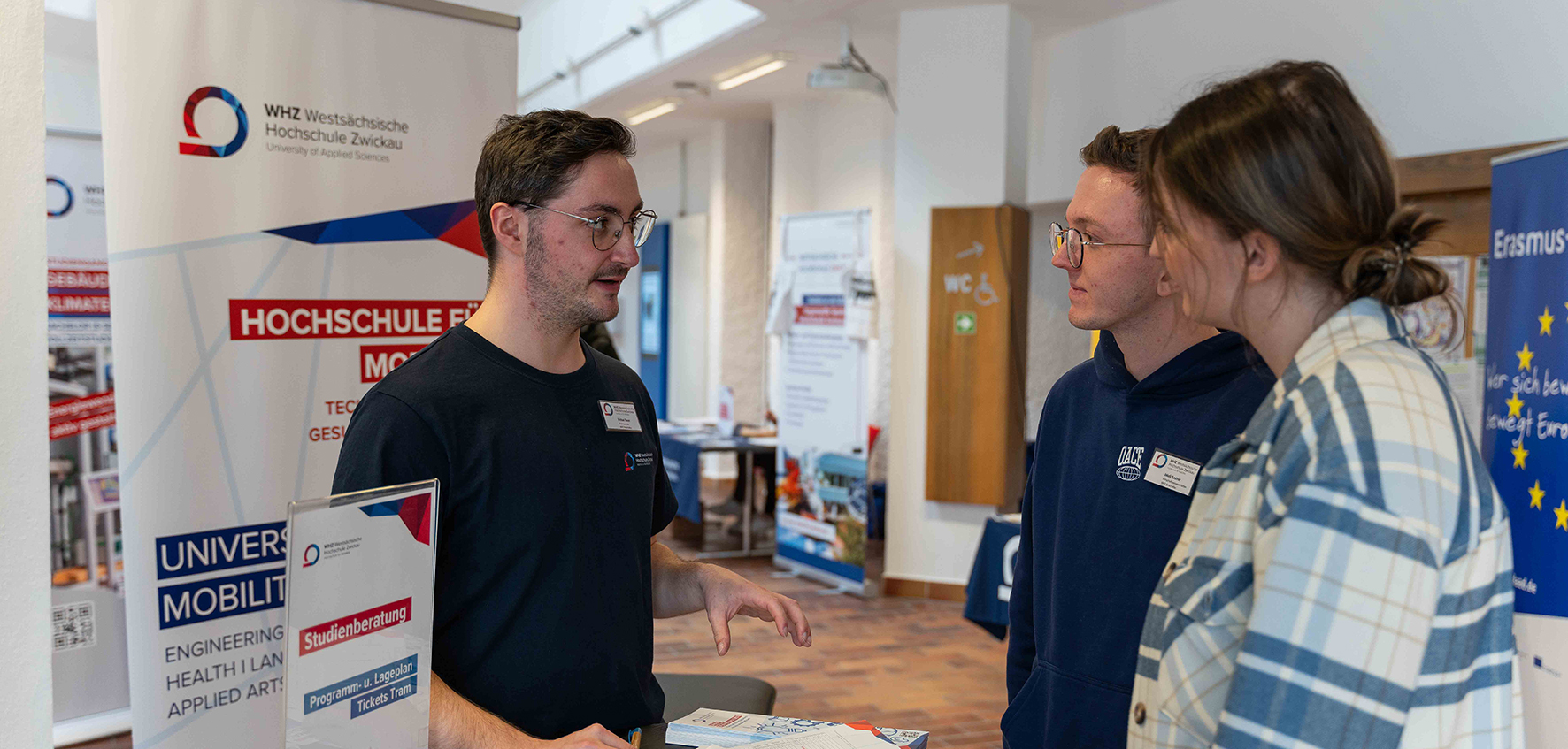 Zwei Personen werden an einem Stand von einem Studierenden beraten.