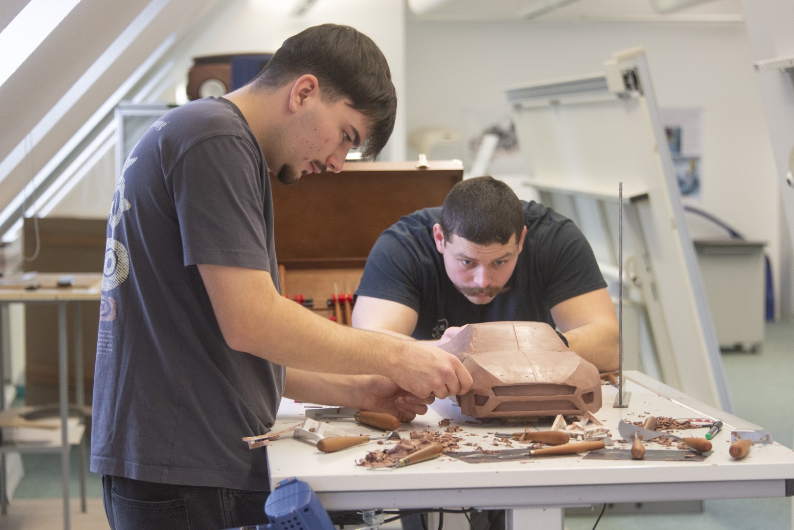 Zwei Studierende schauen konzentriert auf ein Fahrzeugmodell vor sich auf dem Arbeitstisch.