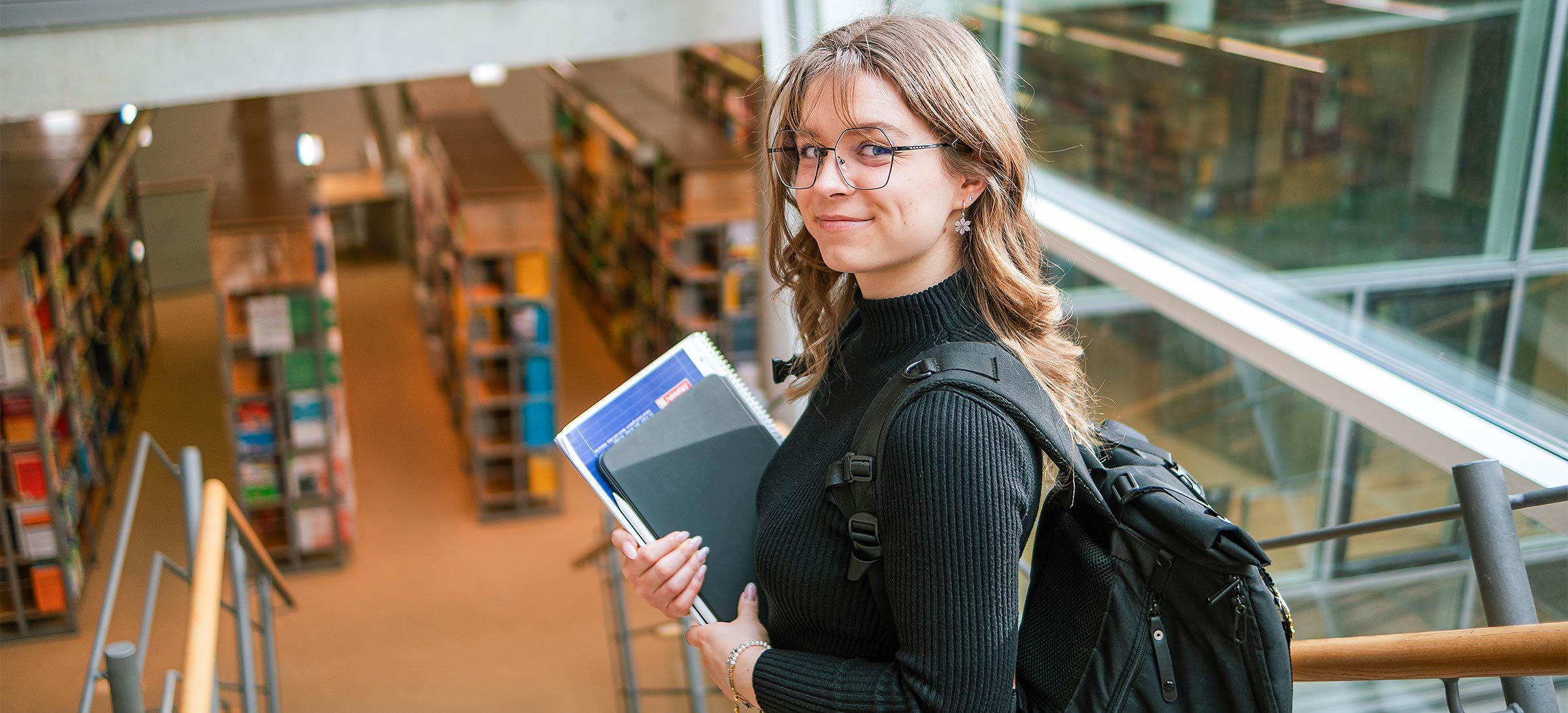 Foto: Studierende in der Hochschulbibliothek der WHZ und lächelt freudig in die Kamera. (Quelle: WHZ/Valentin Hermann)