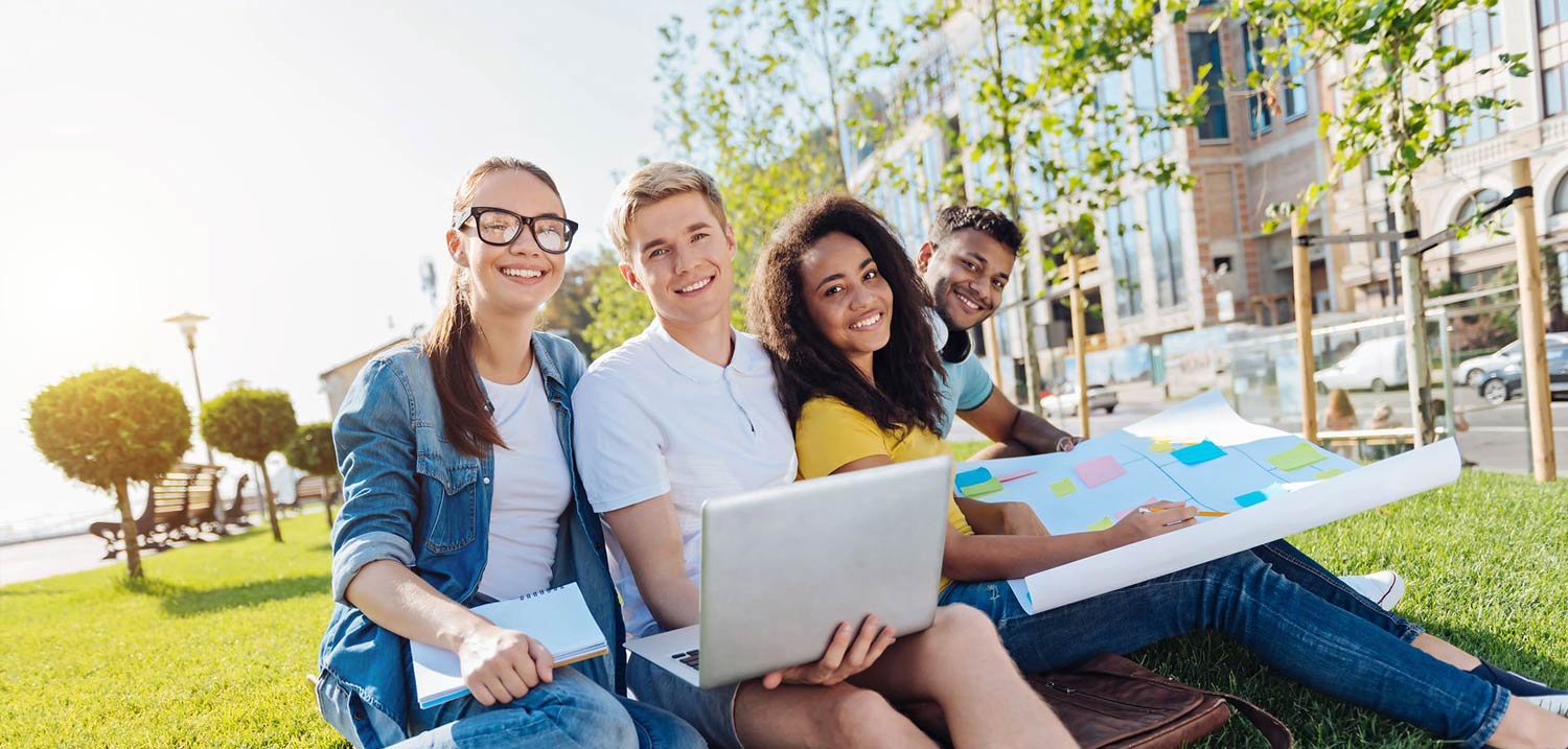 Titelbild Tutorenprogramm. Vier Studierende sitzen draußen zusammen und lächeln in die Kamera. Quelle: zinkevych/fotolia