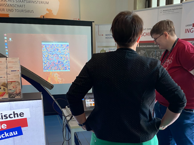 Zwei Frauen schauen auf die Leinwand, auf der das Bild eines Besuchers in Optik eines Gemäldes zu sehen ist