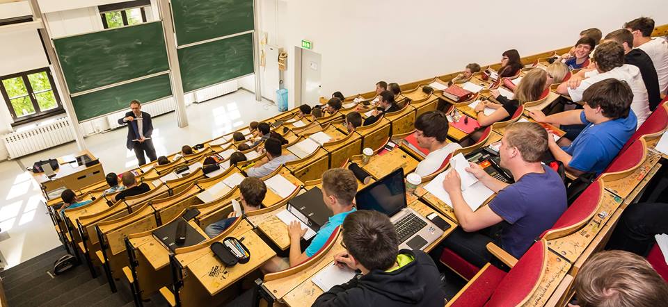 Foto: Studierende sitzen in einem Tivoli Hörsaal und hören einer Vorlesung zu.