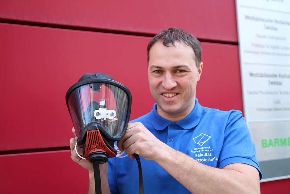 Foto: Prof. Herold zeigt eine Feuerwehrmaske mit Datenbrille in die Kamera.