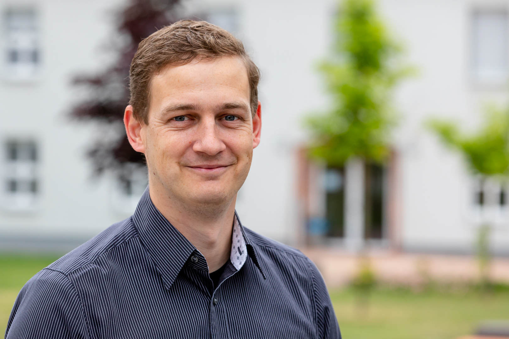 Prof. Laroque lächelt in die Kamera, im Hintergrund der Campus der Hochschule
