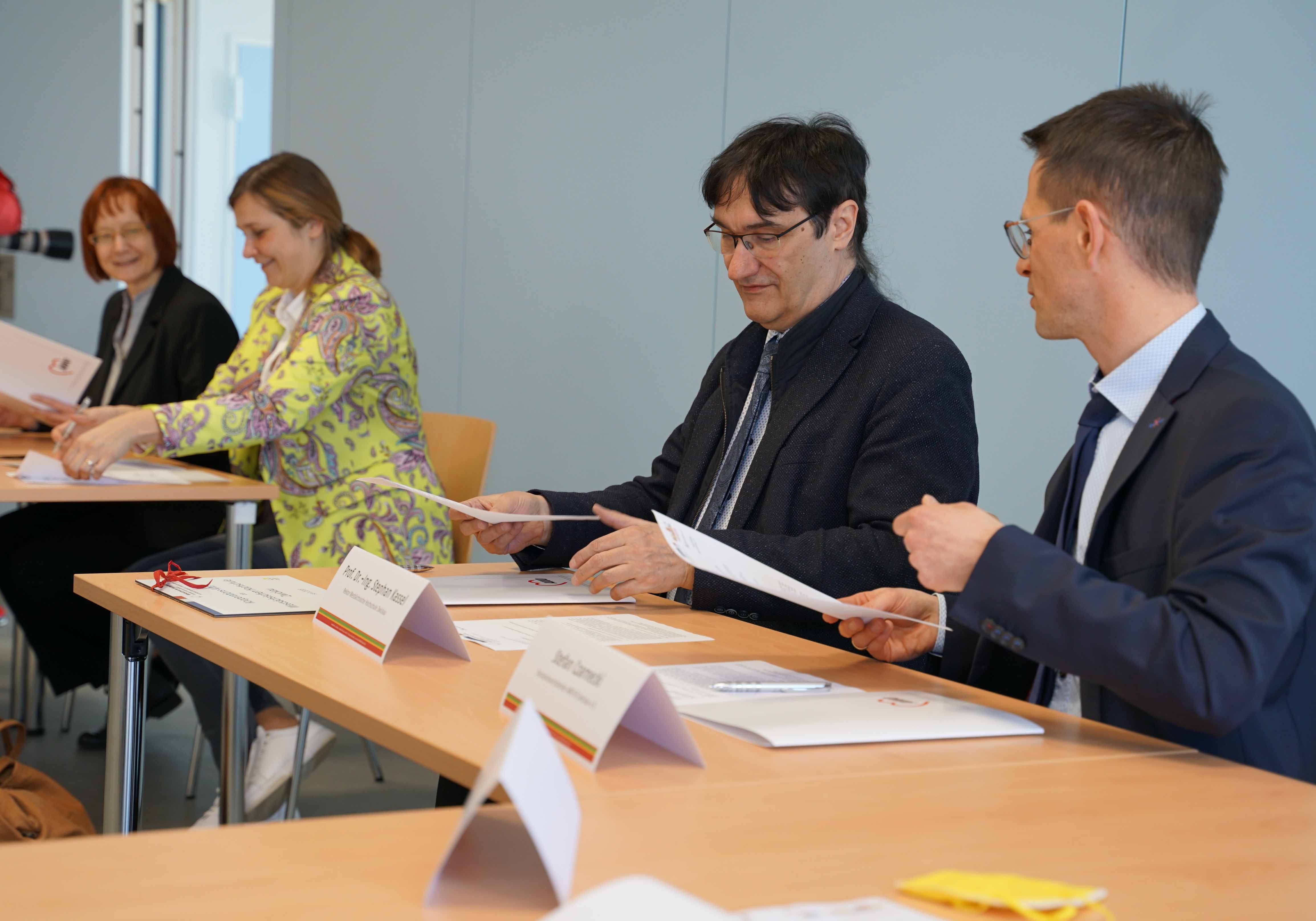 Die Vertragspartner sitzen an Tischen und unterzeichnen Vertragsuntwerlagen.