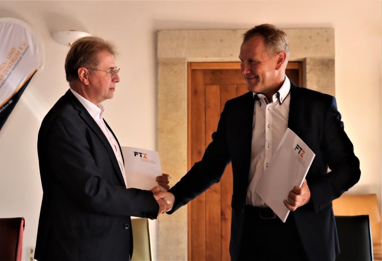 Zwei Männer schütteln sich die Hände, jeder von ihnen hält eine Mappe in der Hand.