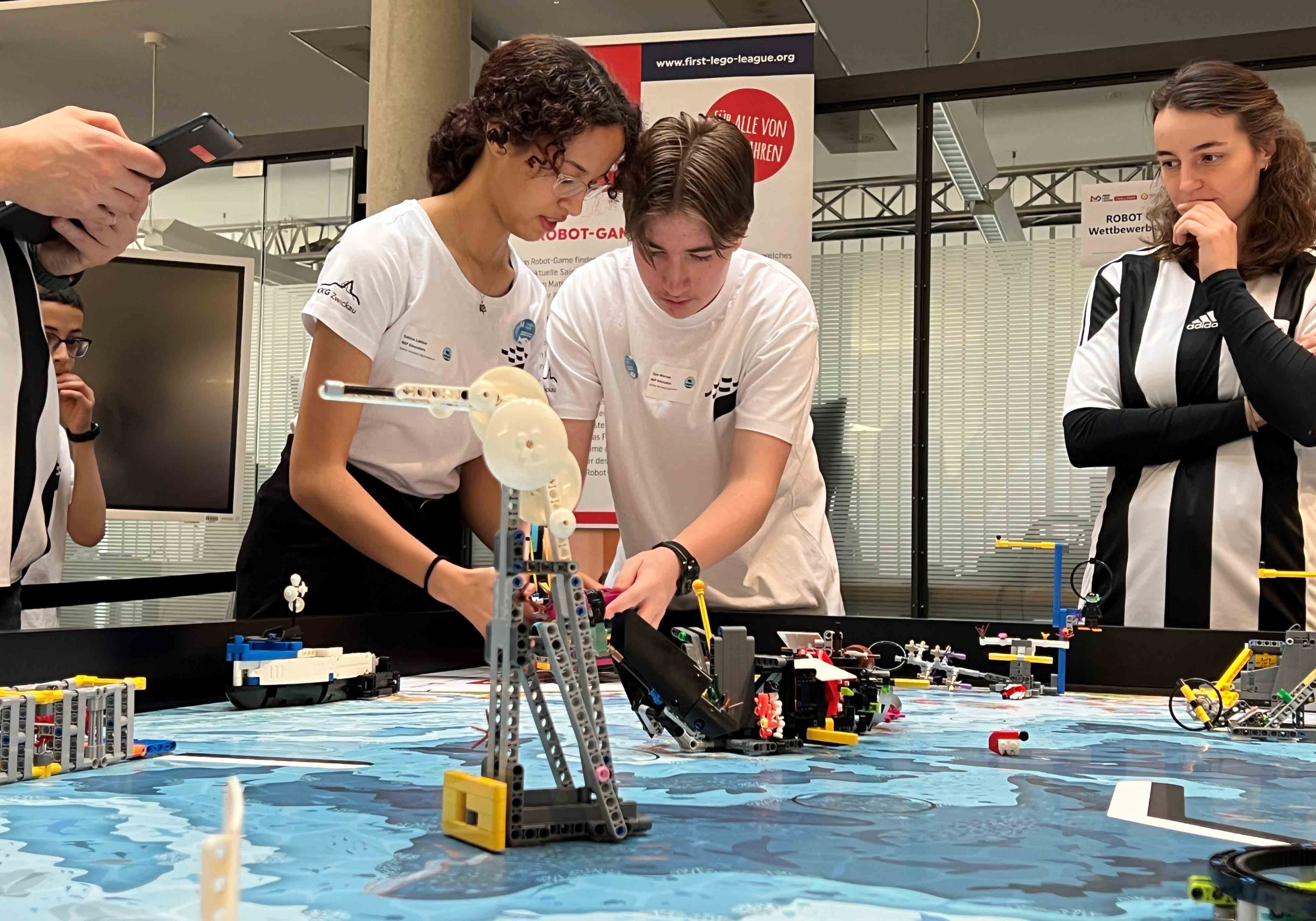Eine Schülerin udn ein Schüler schauen konzentriert auf einen Lego Spieltisch. 