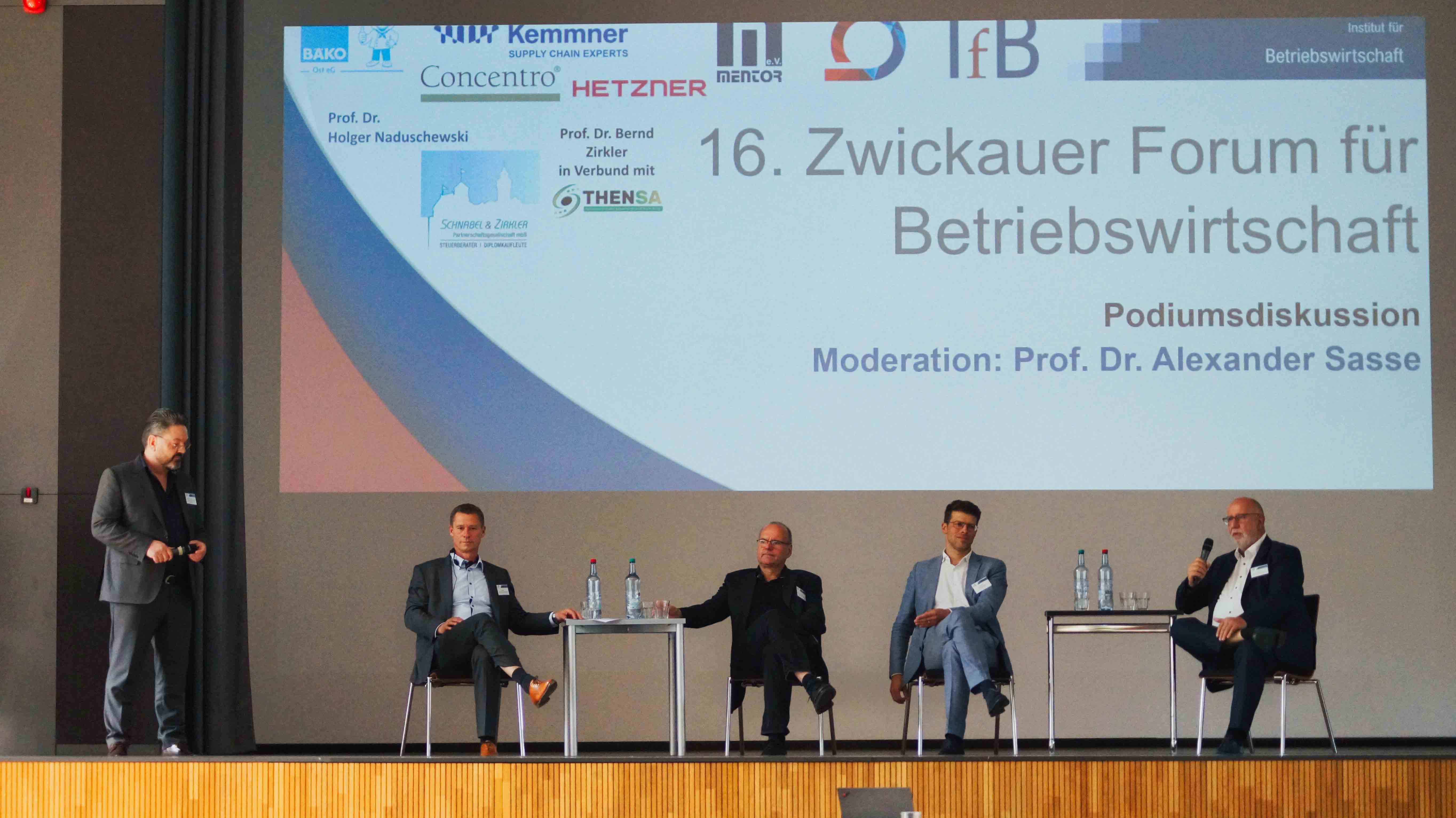 Personen sitzen auf einer Bühne und diskutieren. 