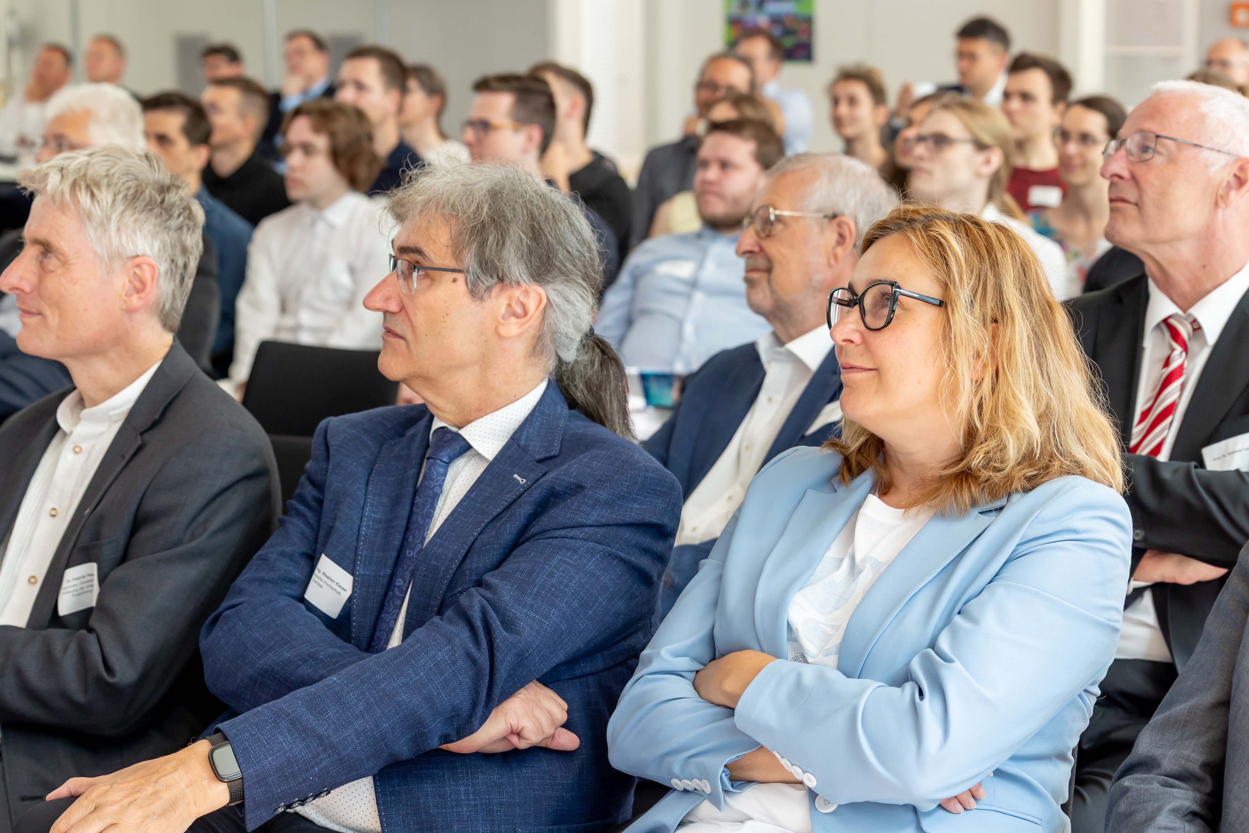 Oberbürgermeisterin und Hochschulrektor sitzen in einem vollbesetzten Saal und verfolgen einen Vortrag. 