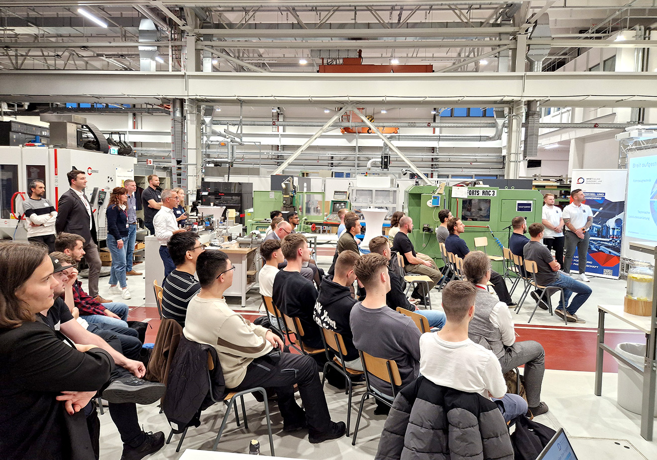 Studierende sitzen in einer Werkhalle und verfolgen einen Vortrag. 