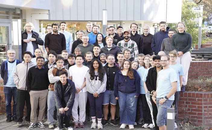 große Gruppe von jungen Menschen steht draußen vor der Mensa und schaut in die Kamera