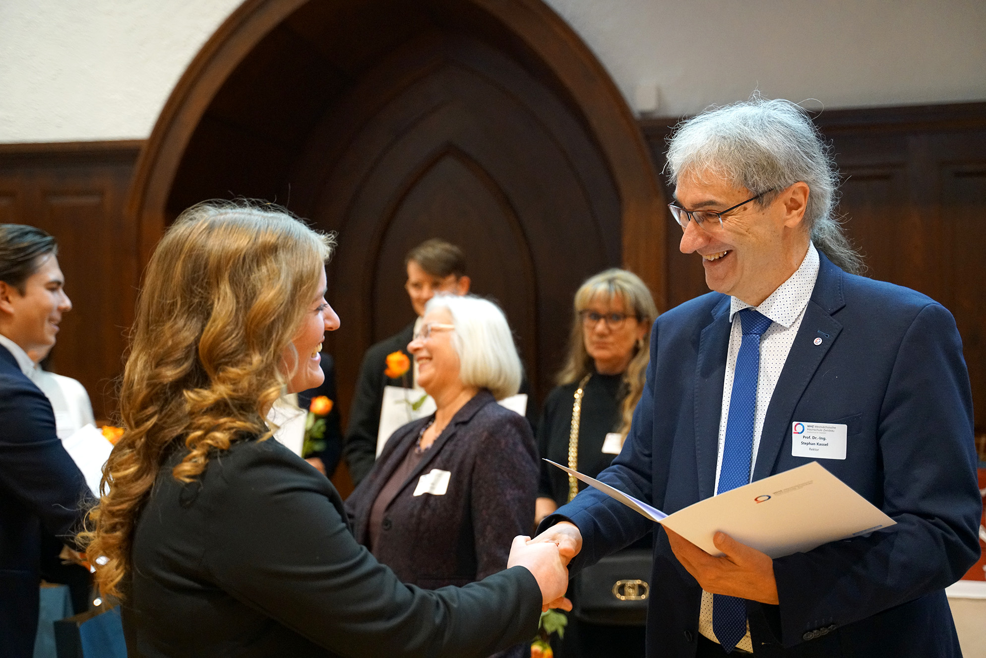 Rektor Prof. Stephan Kassel übergibt eine Urkunde an eine Stipendiatin. 