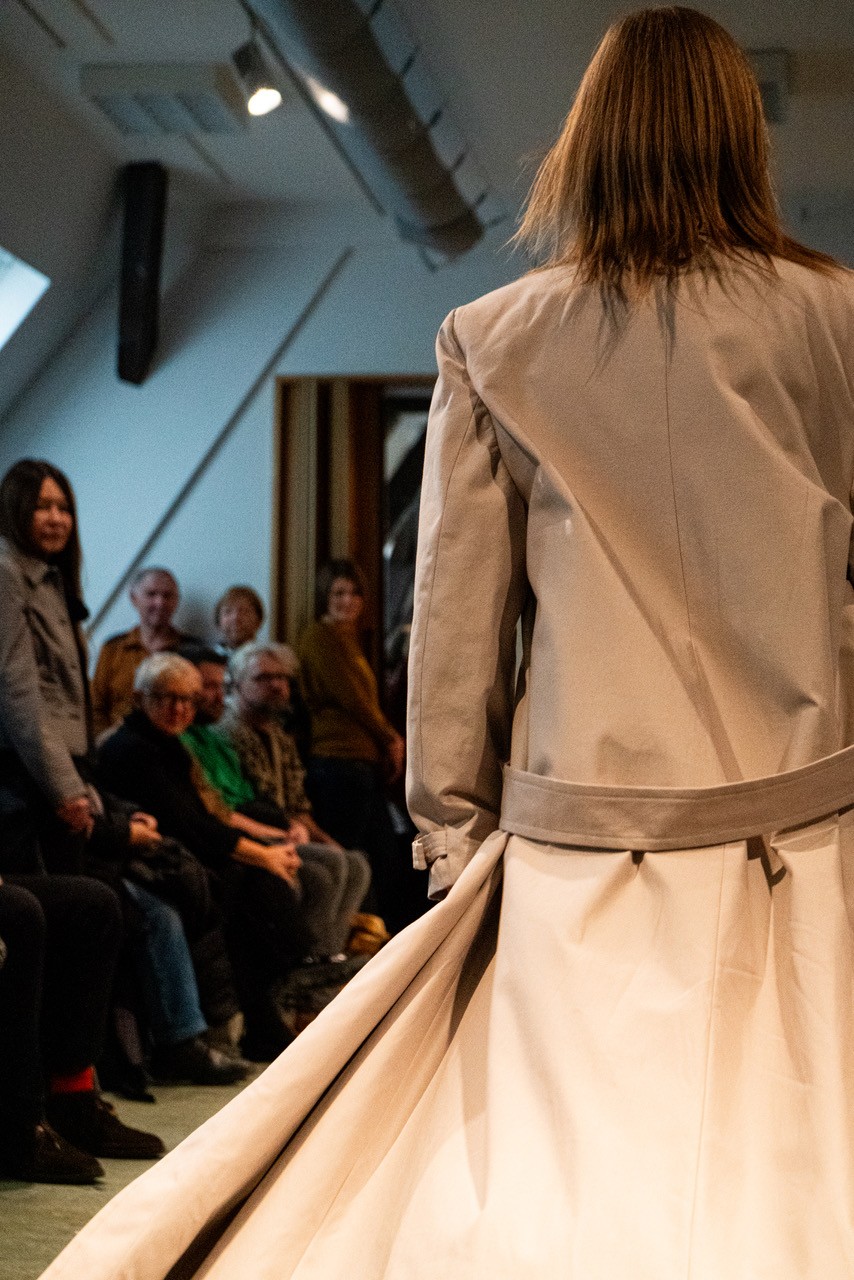 Ein Model läuft über in einem eleganten Mantel über den Laufsteg. 