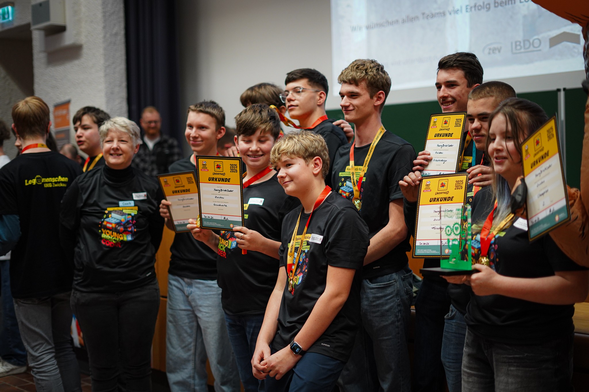 Eine Gruppe junger Menschen hält freudig ihre Urkunden in der Hand. Daneben steht stolz die Lehrerin.