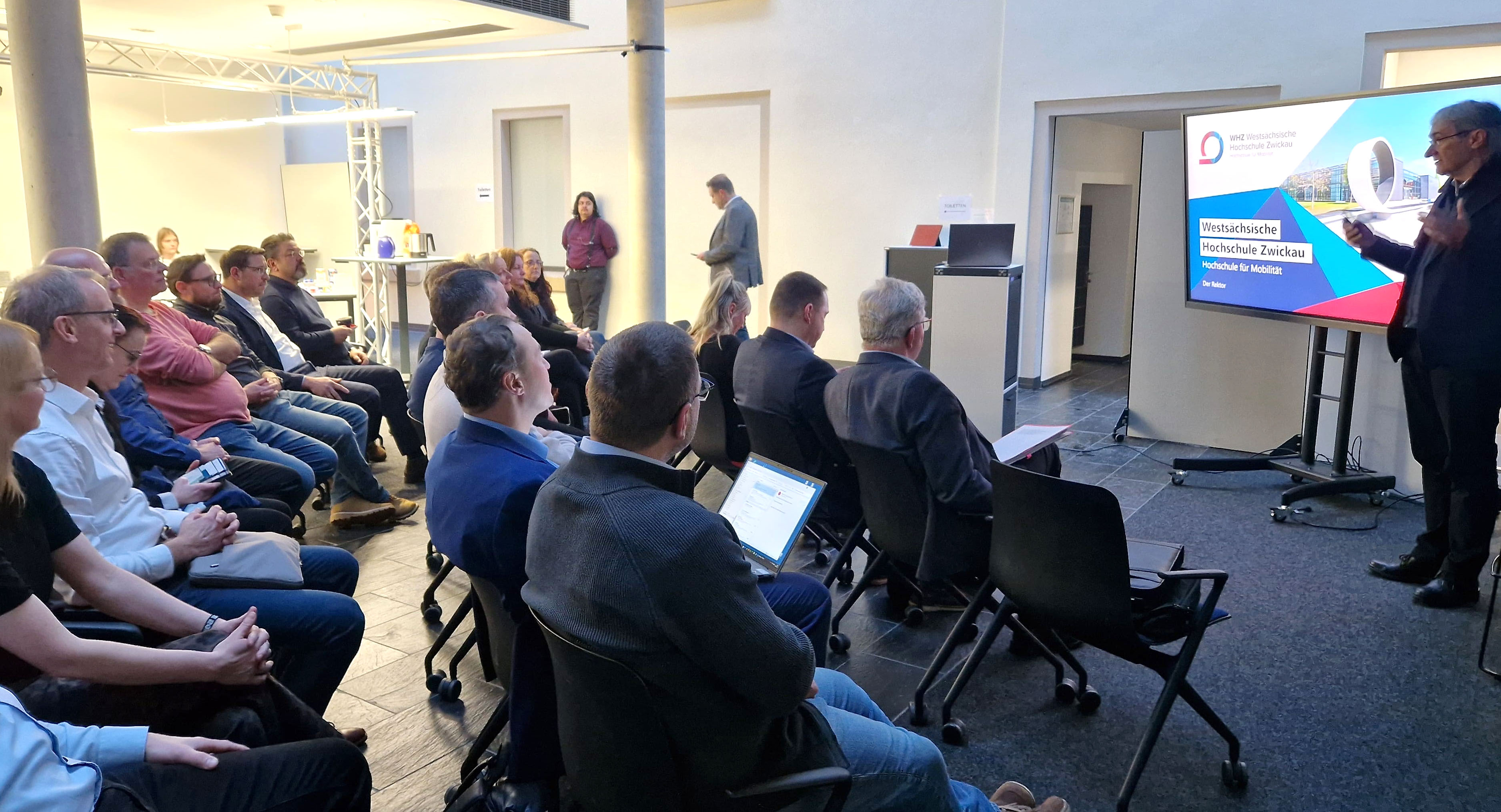 Gäste verfolgen einen Vortrag des Rektors. 