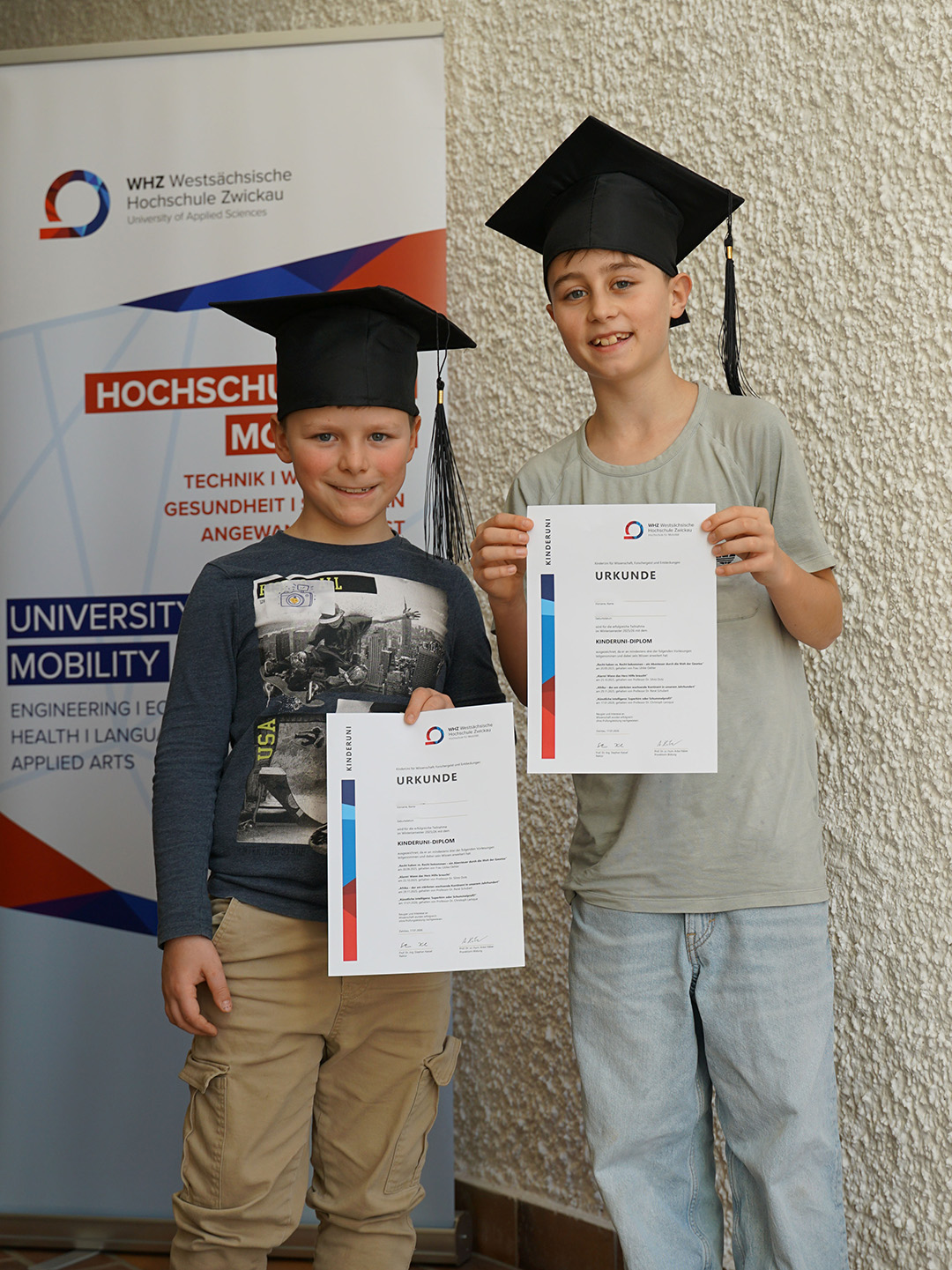 Zwei Kinder präsentieren ihre KinderUni-Diplome. 