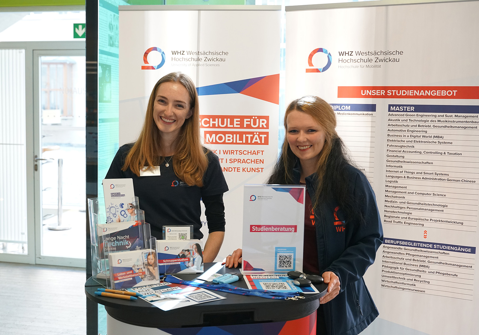 Zwei Studienberaterinnen stehen an einem Infostand. 