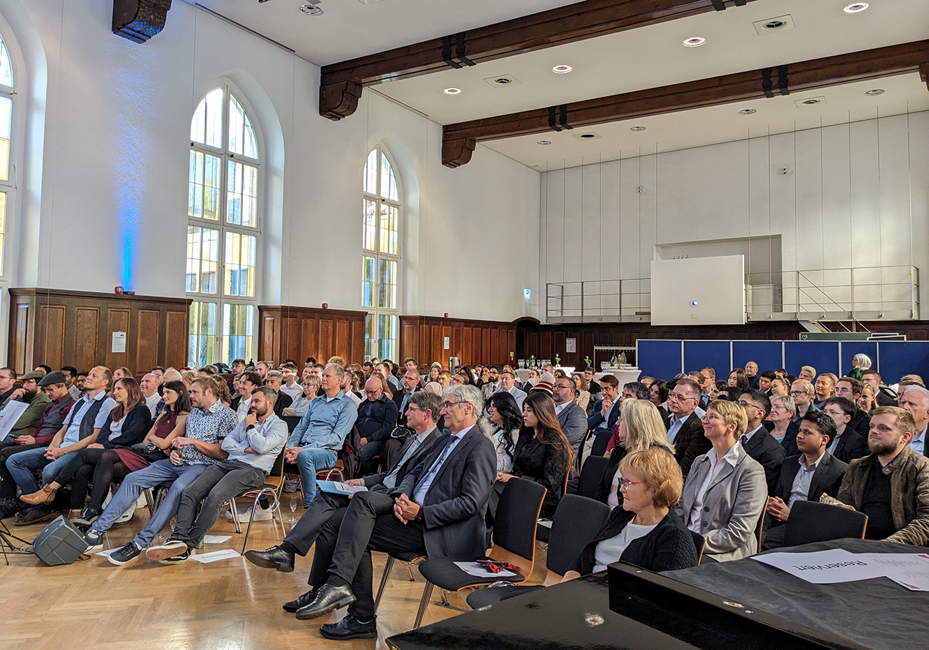 Personen sitzen in einem festliches Saal. 
