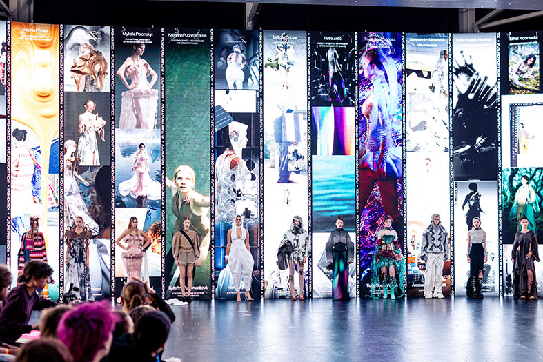 Models präsentieren Kollektionen vor einer Leinwand mit digitalen Bildschirmen. 