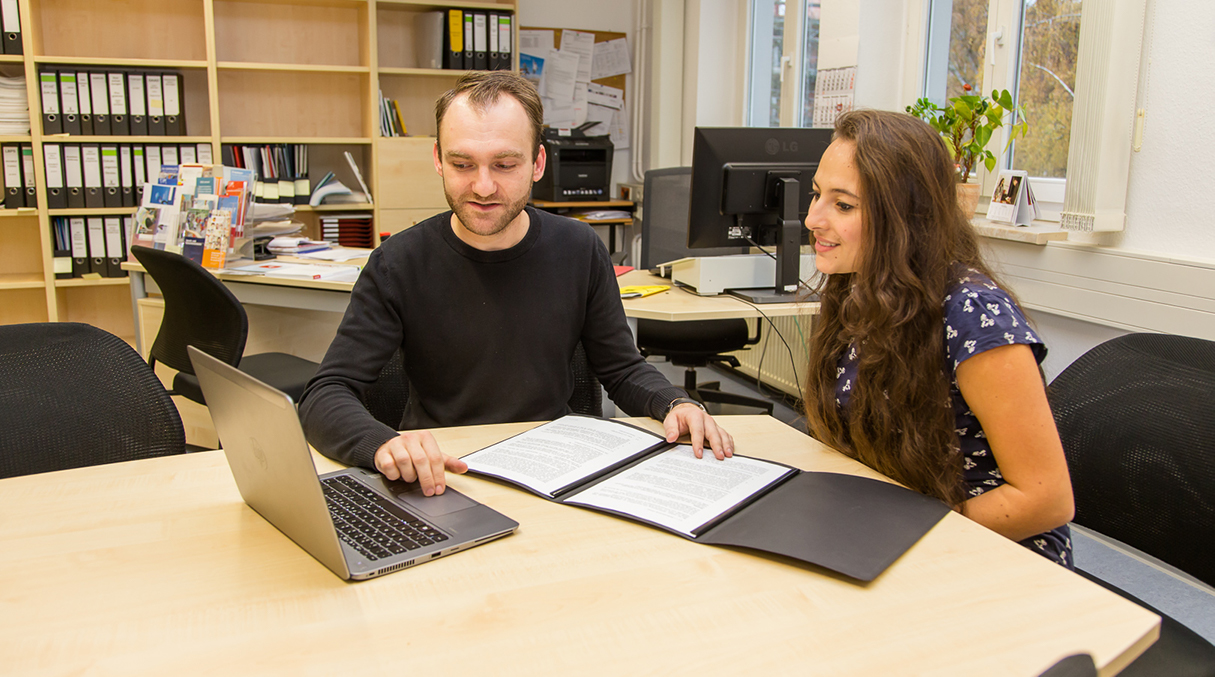 An einem Tisch sitzend berät ein Studienberater eine Studieninteressentin.