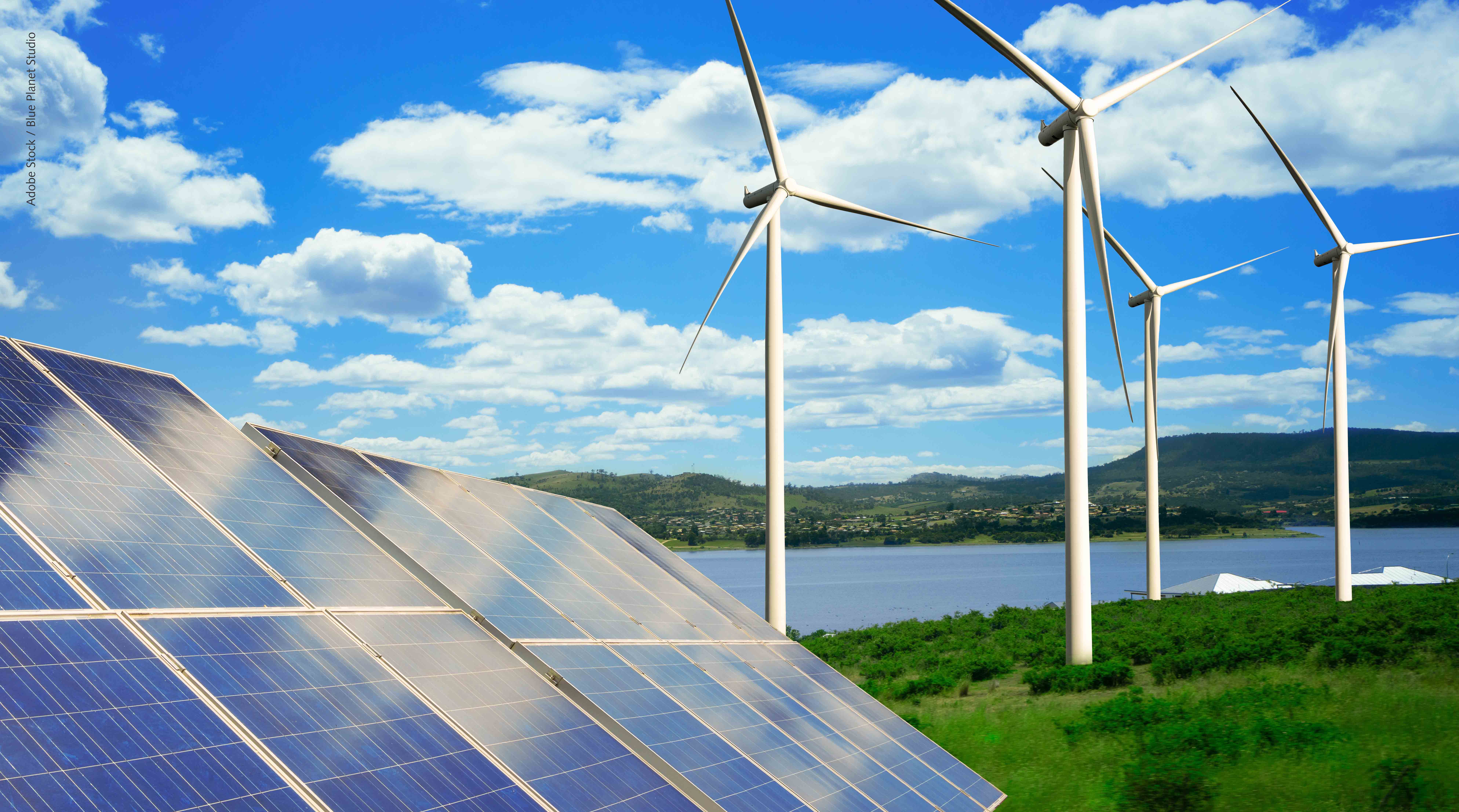 Foto: Eine Landschaft mit See und leicht bewölkten Himmel. Im Vordergrund sind Solarkollektoren und dahinter versetzt Windräder dargestellt.