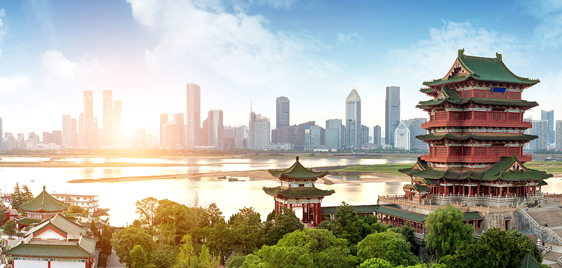 Foto: Blick auf ursprüngliche chinesische Architektur. Dahinter ein breiter Fluss und am anderen Ufer eine Skyline mit Hochhäusern.