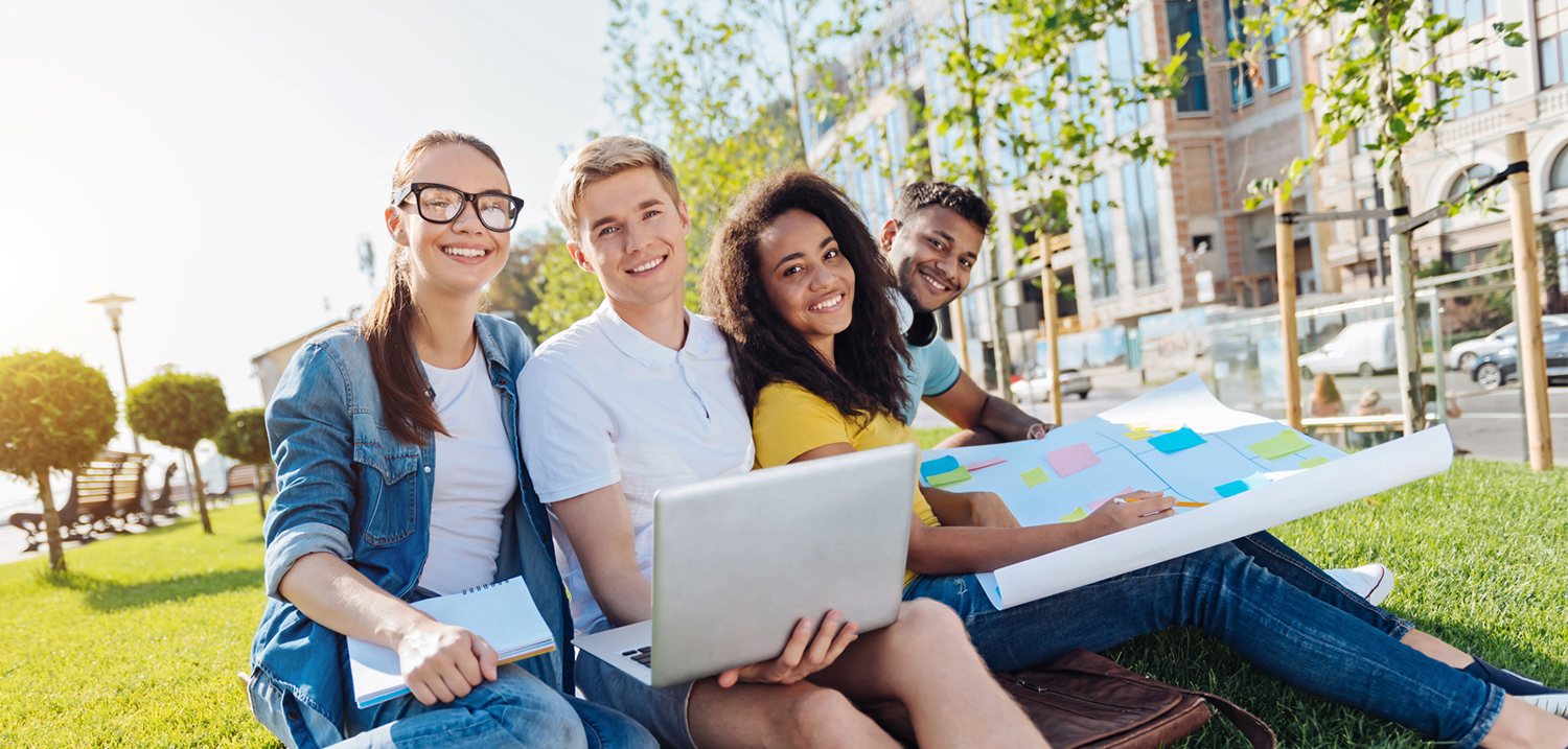 Internationale Studierende sitzen auf einer Wiese und lächeln in die Kamera. 