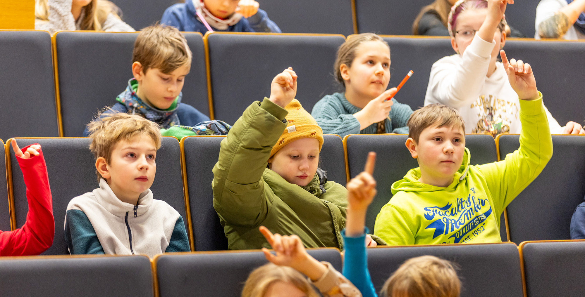 Kinder im Hörsaal heben ihre Hände