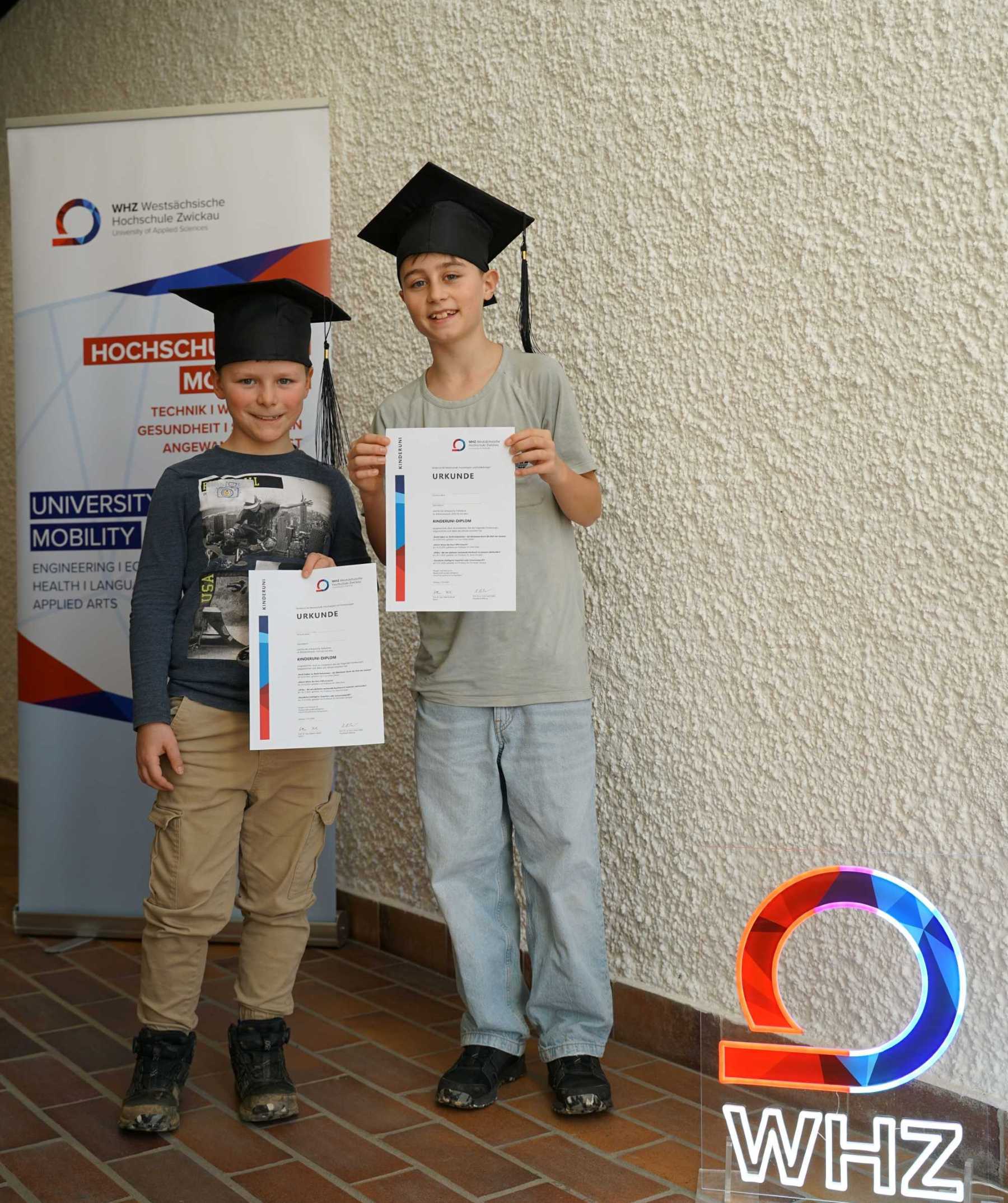 KinderUni Abschluss 2026, zwei Jungen zeigen stolz ihre KinderUni-Diplome
