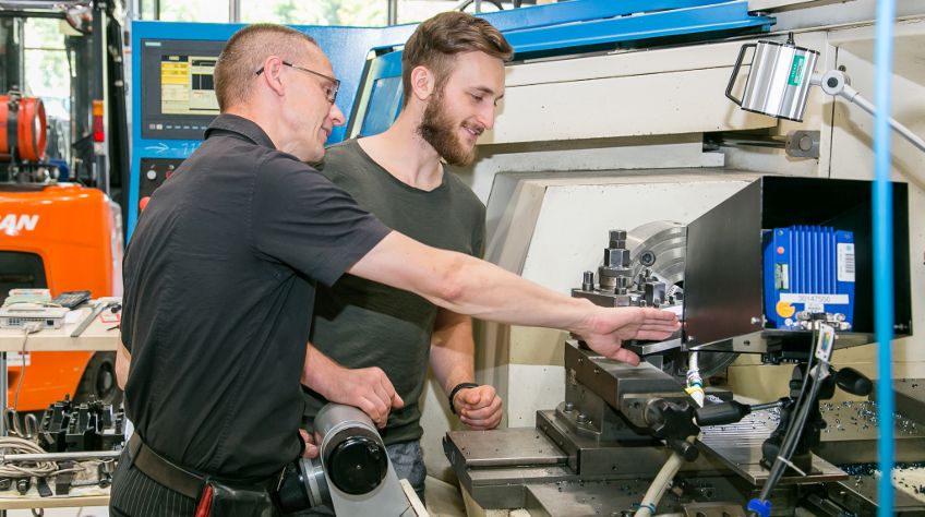 Foto: Ein Studierender erhält von einem Lehrenden eine Einweisung an einer Maschine.
