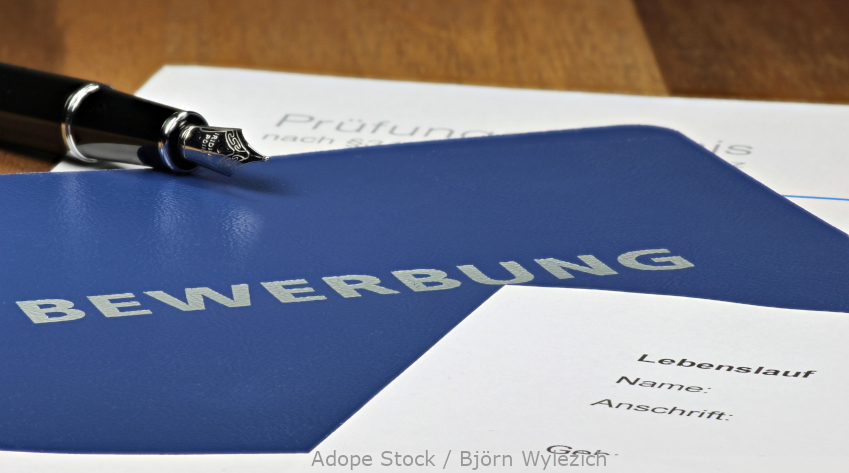 Foto: Deckumschlag mit der Aufschrift "Bewerbung" liegt auf einem Tisch.