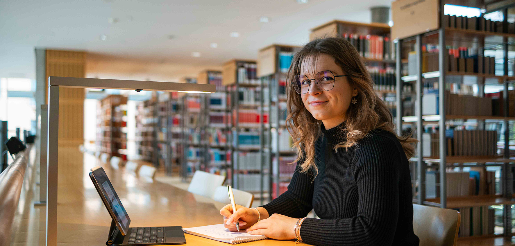 Eine Studierende sitzt in der Bibliothek vor einem Laptop. 